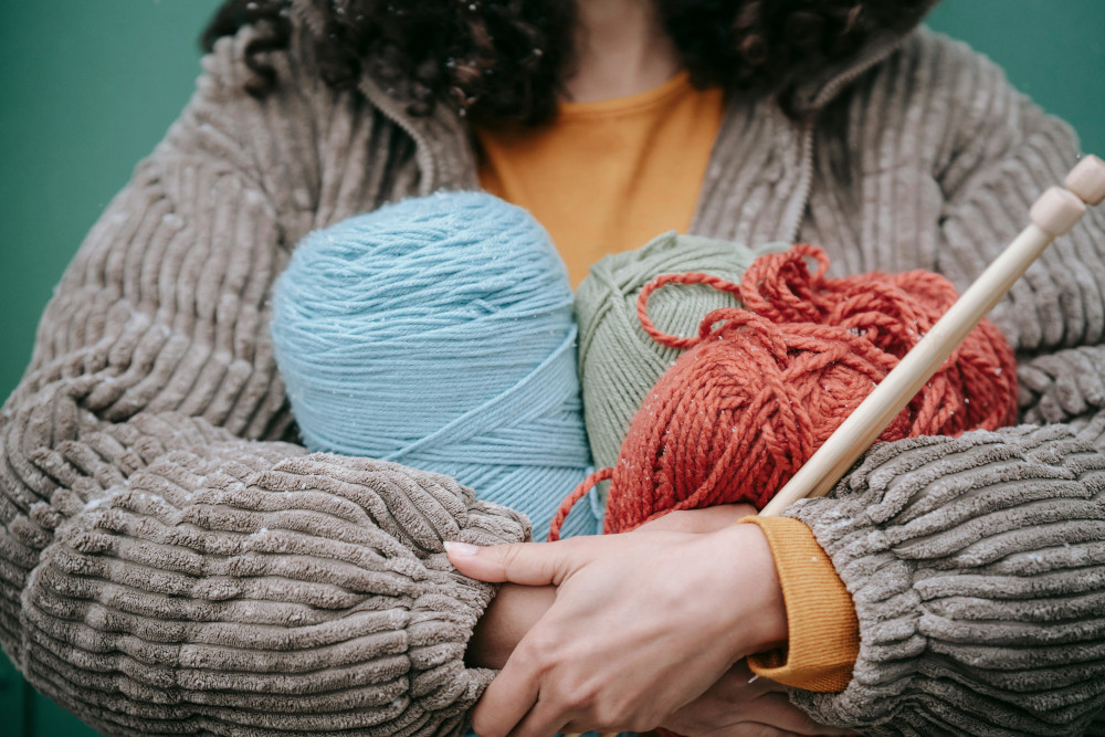 woman holding 3 large skeins of yarns and knitting needles